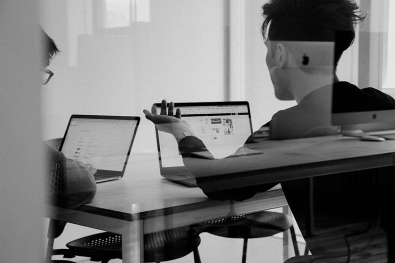 Two individuals seated at a table, each using a laptop, engaged in a discussion about AI deployment tools.